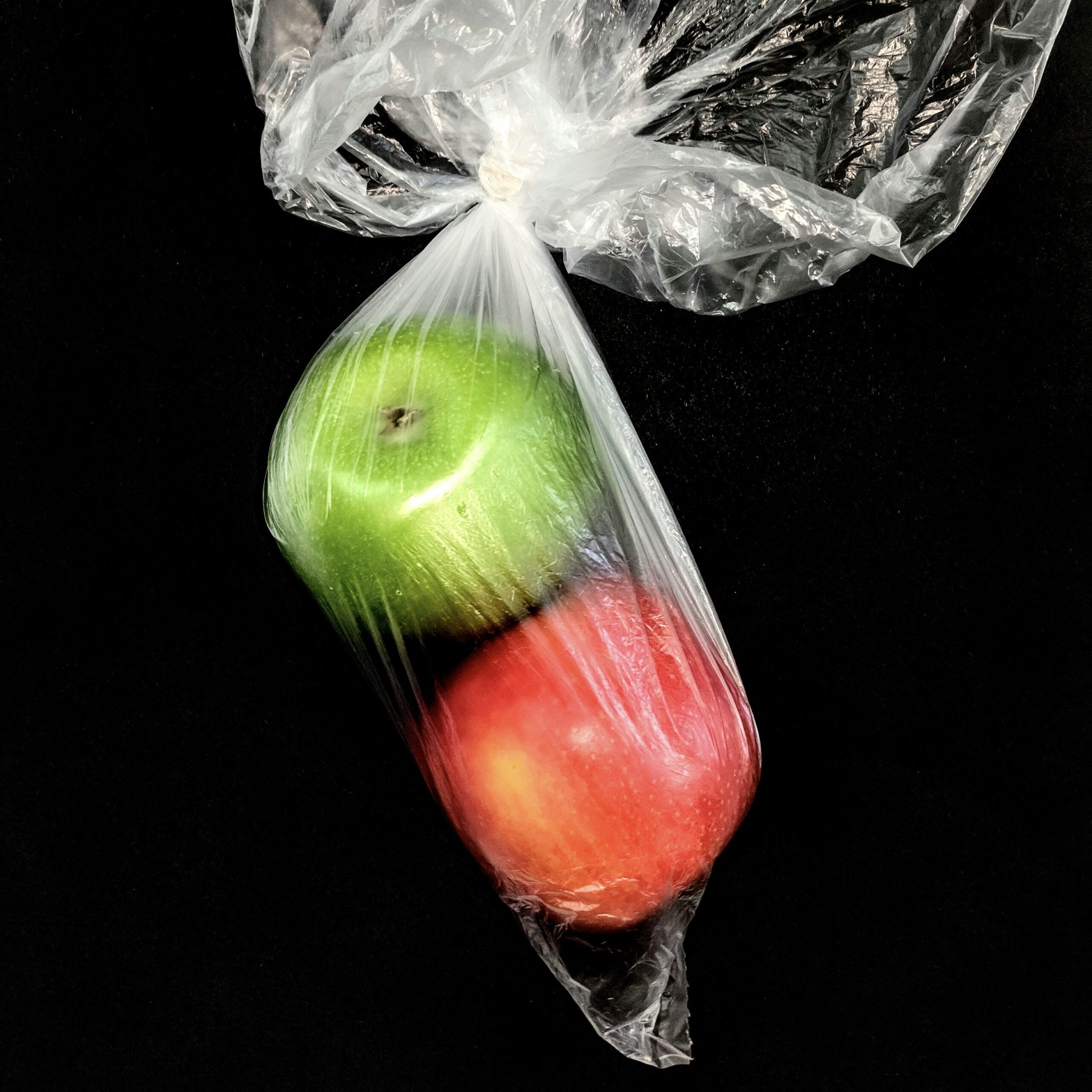 Plastic bag of two red and green apples, black background.